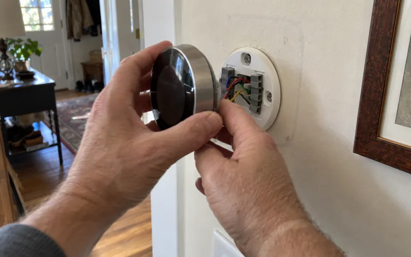 Removing a round smart thermostat from its base to reveal the wires