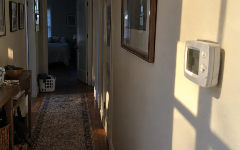 Wall thermostat in a hallway with direct afternoon sunlight falling on it
